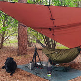 DD Hammocks Magic Carpet providing shelter in a campsite with a black dog nearby.